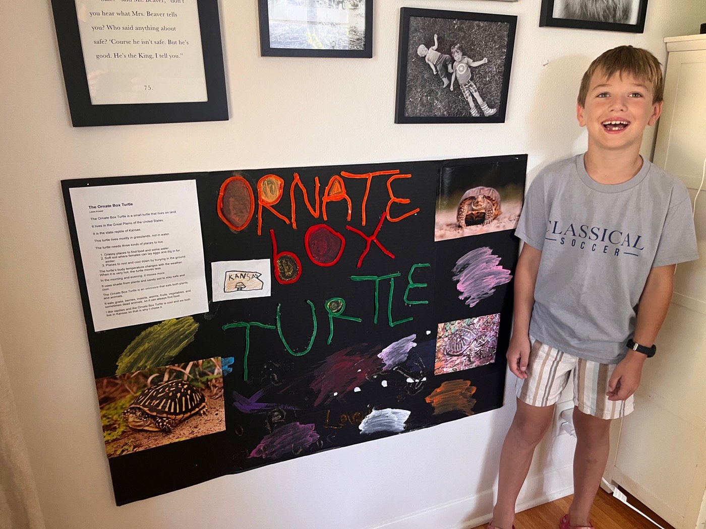 Lewis standing beside his school poster board, "Ornate Box Turtle" written in red and green marker, with photographs of box turtles and his written report pinned to the black board