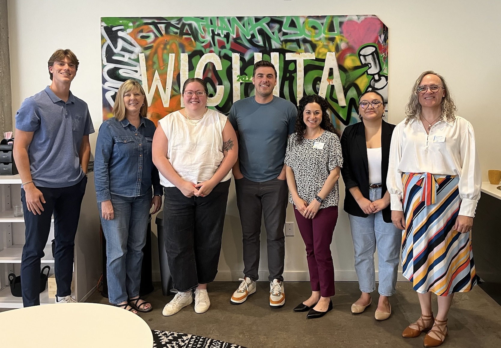 Group photo of seven cohort participants standing in front of a colorful "WICHITA" graffiti mural